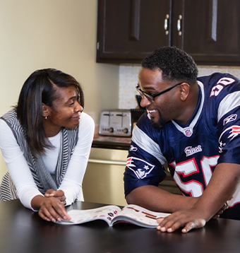 An African American couple takes a break from reading a magazine to gaze into each others eyes and smile. 