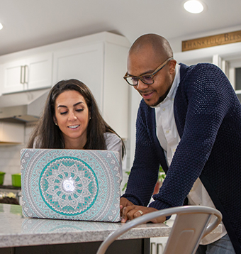A mixed race couple searches their laptop on their kitchen island.
